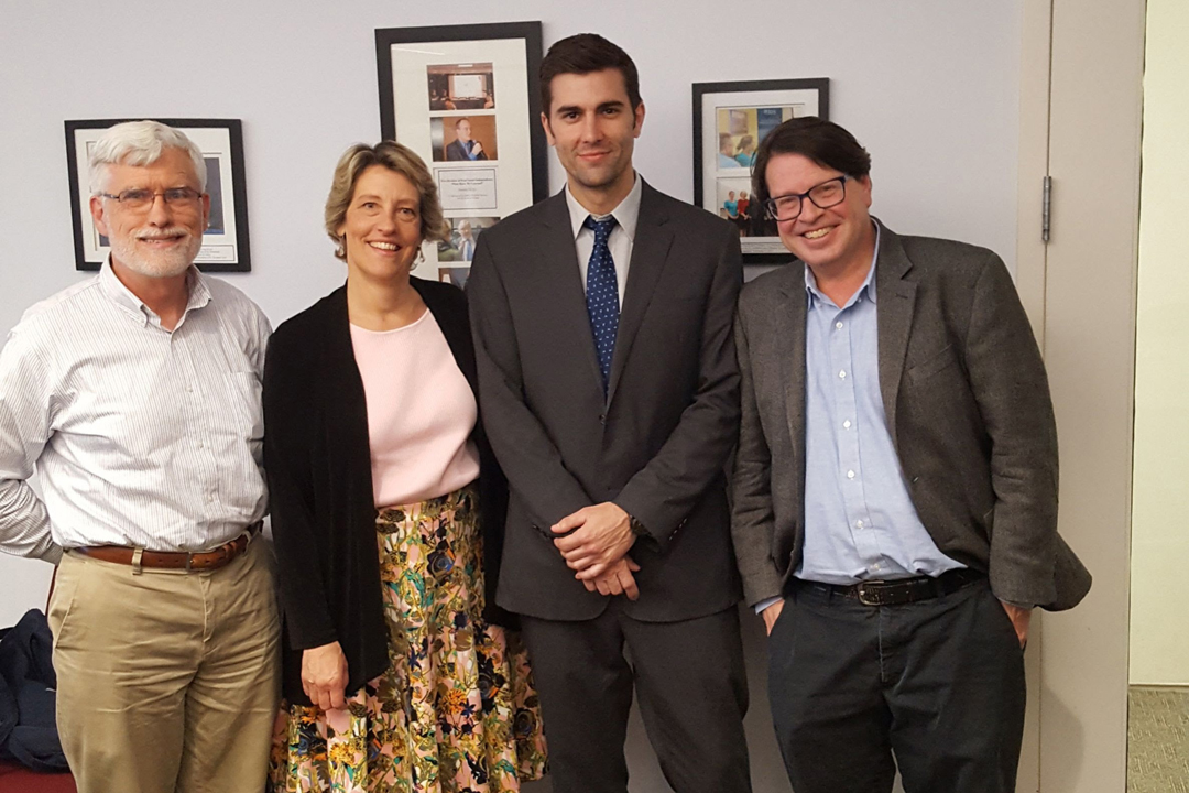 Three History Department faculty members standing with new PhD Mark Alexander after his dissertation defense.