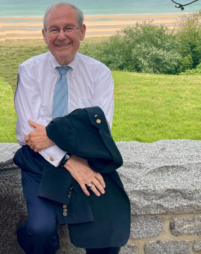 Tom Long sitting on a stone bench in front of a beach