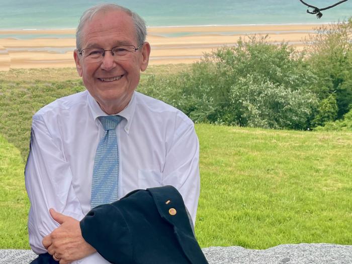 Tom Long sitting on a stone bench in front of a beach